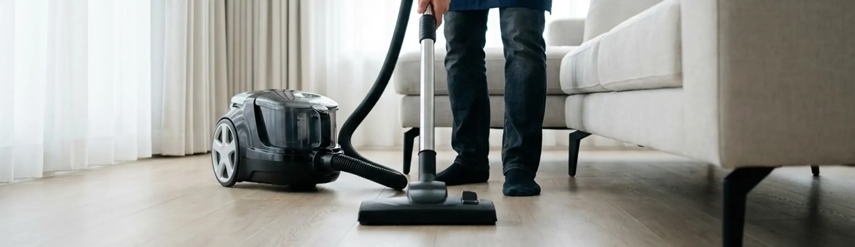 Professional house cleaner vacuuming a living room floor with a canister vacuum cleaner, New Orleans, LA.