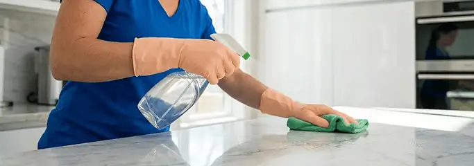 Maid service worker spraying and wiping a kitchen countertop with a microfiber cloth for sanitizing, New Orleans, LA.
