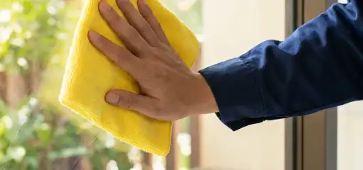 House cleaner wiping a glass window with a yellow microfiber cloth for streak-free cleaning, New Orleans, LA.